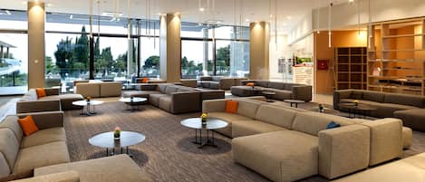 A spacious lobby with multiple seating areas, large windows, and a modern interior design.