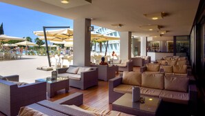 Un amplio espacio lounge al aire libre con mobiliario de mimbre, sombrillas y una piscina al fondo.