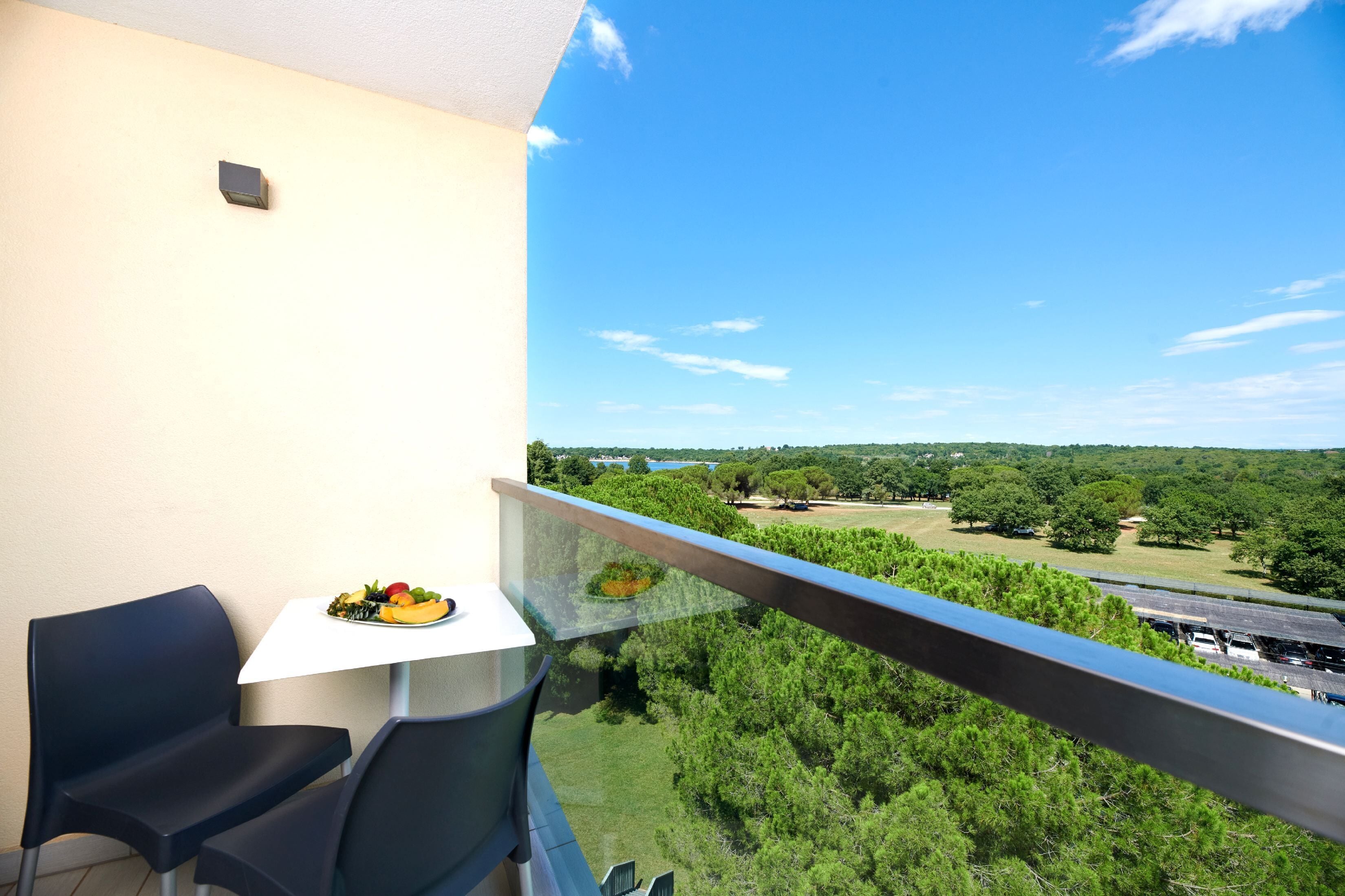 Varanda com mesa e cadeiras, com vista para uma paisagem verde com árvores e um corpo de água.