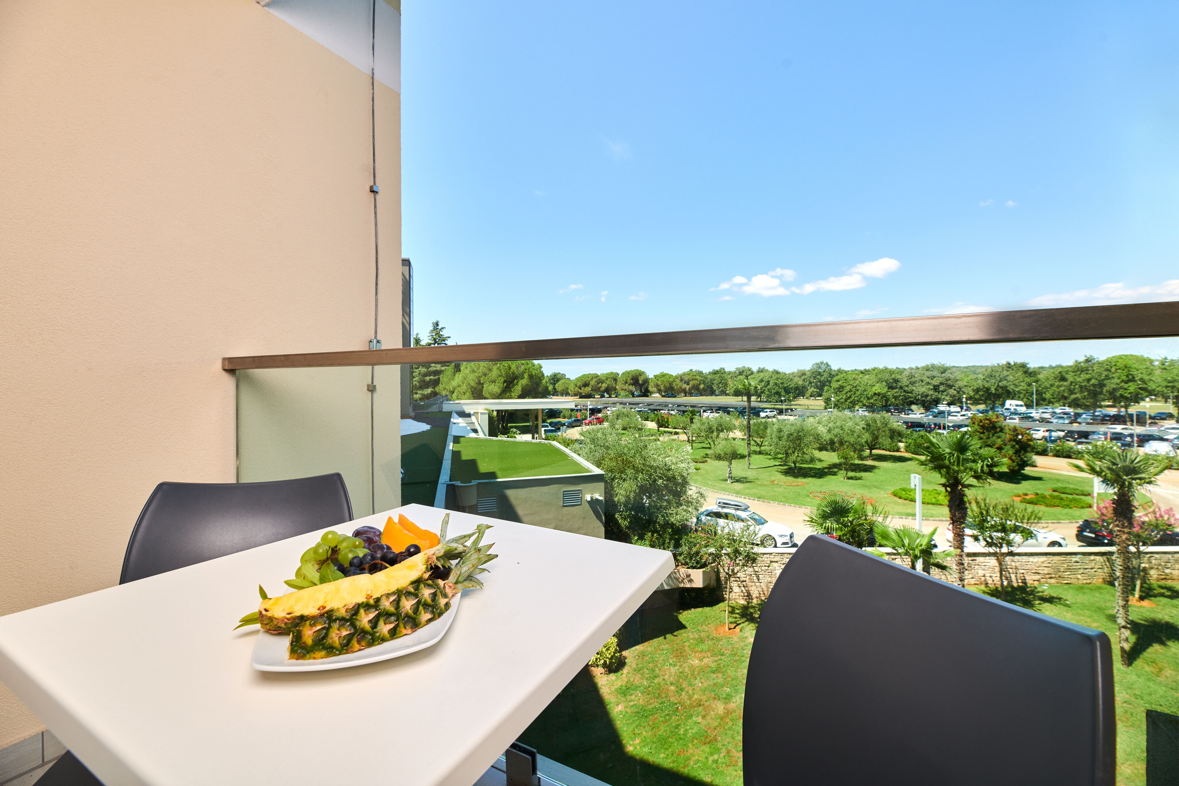 Balcón con una mesa dispuesta para comer, con vistas a un aparcamiento y zonas verdes.