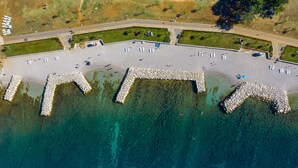 Vista aérea de un paseo marítimo costero con una serie de muelles de piedra que se adentran en el agua, un camino pavimentado y zonas verdes con bancos.