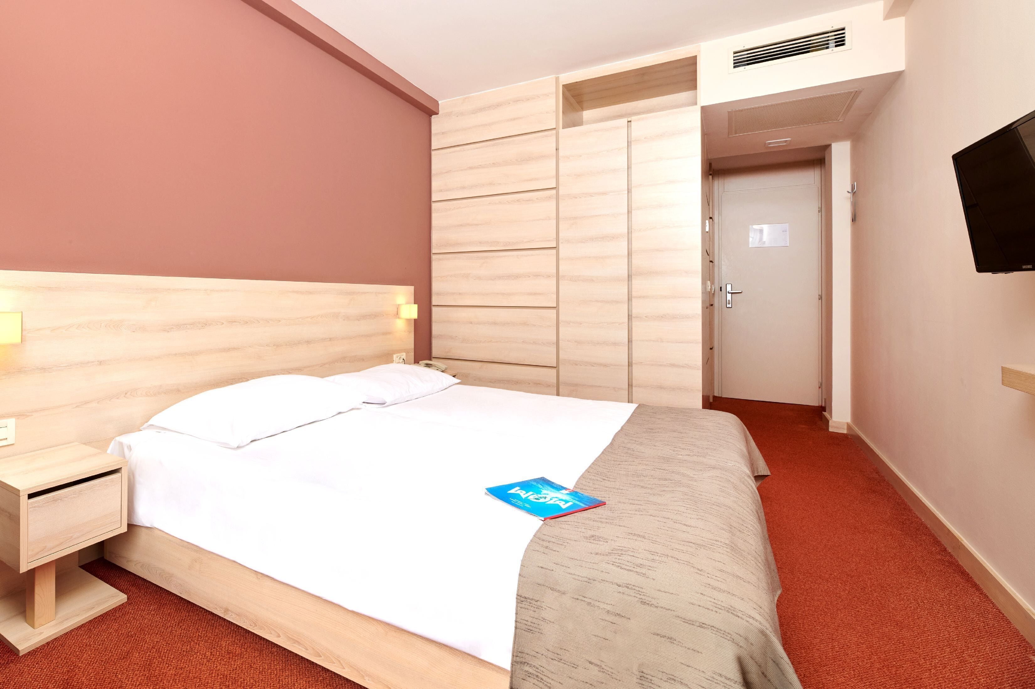 Una habitación de hotel con cama, mesita de noche, televisor montado en la pared y armario.