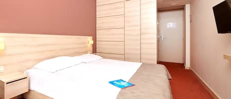 A hotel room with a bed, a bedside table, a TV mounted on the wall, and a wardrobe.