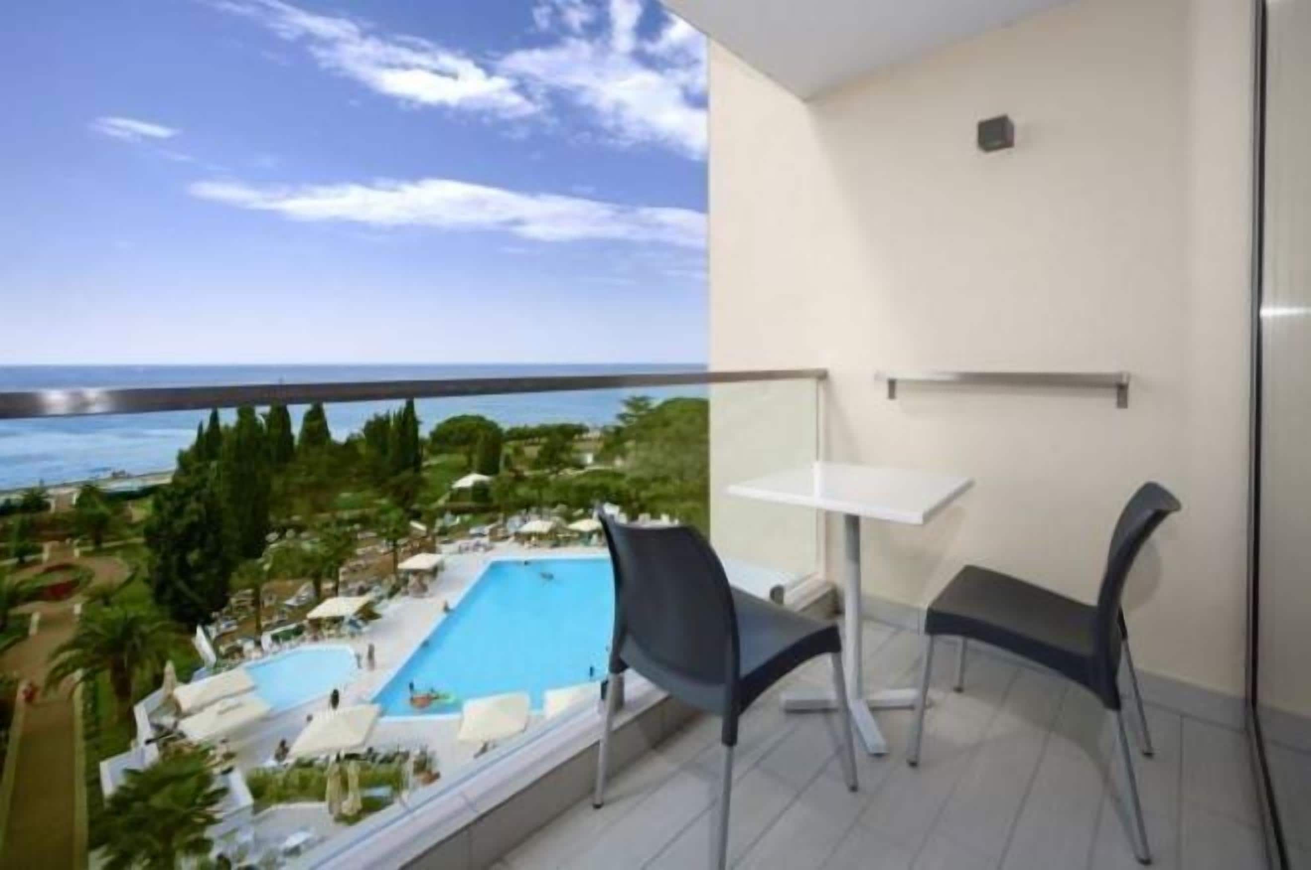 A balcony with a pool view, a table, and two chairs.