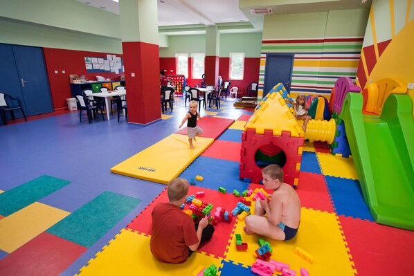 Zona de juegos con colchonetas de colores, bloques de espuma y una casita.
