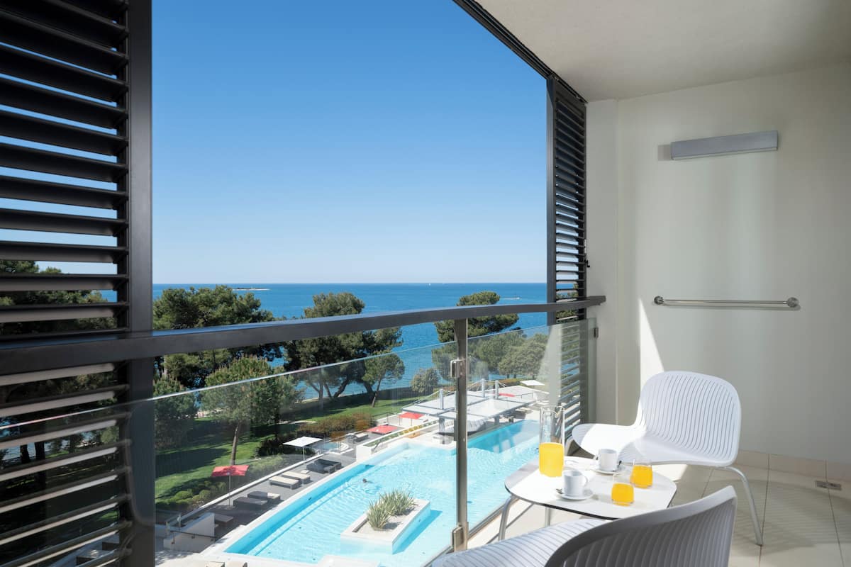 A balcony with a view of a swimming pool and the sea.
