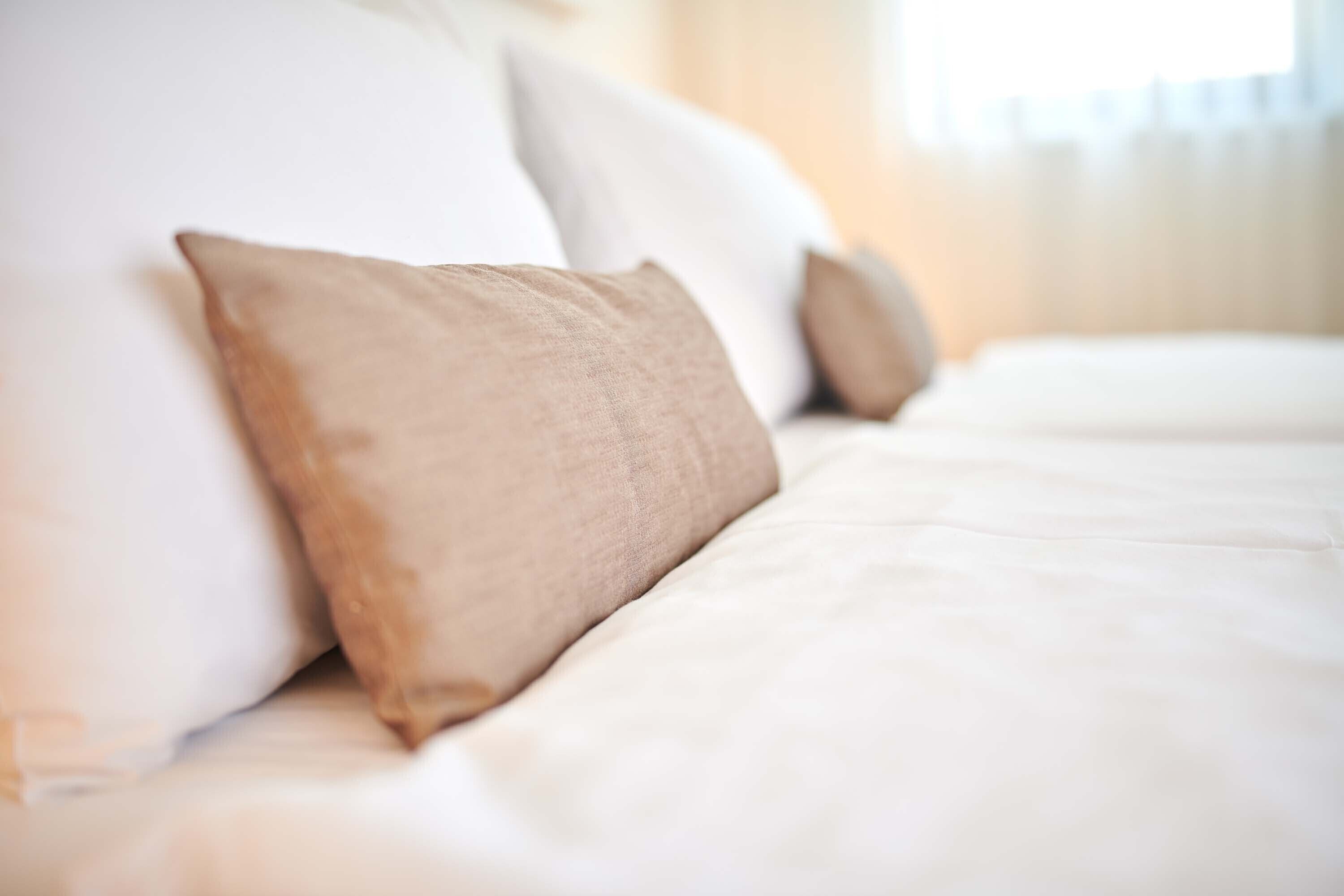 A bed with white bedding and two beige pillows.