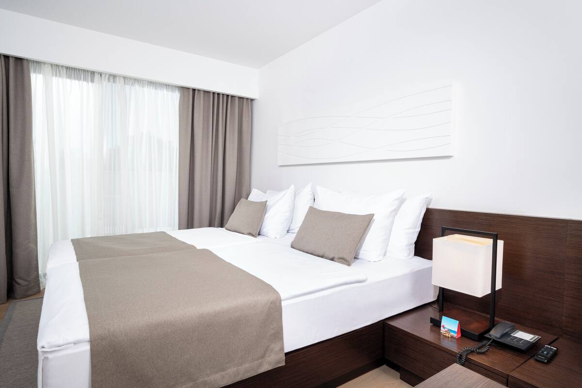 A neatly made bed with a white and brown bedspread, a bedside table with a lamp, and a framed picture.