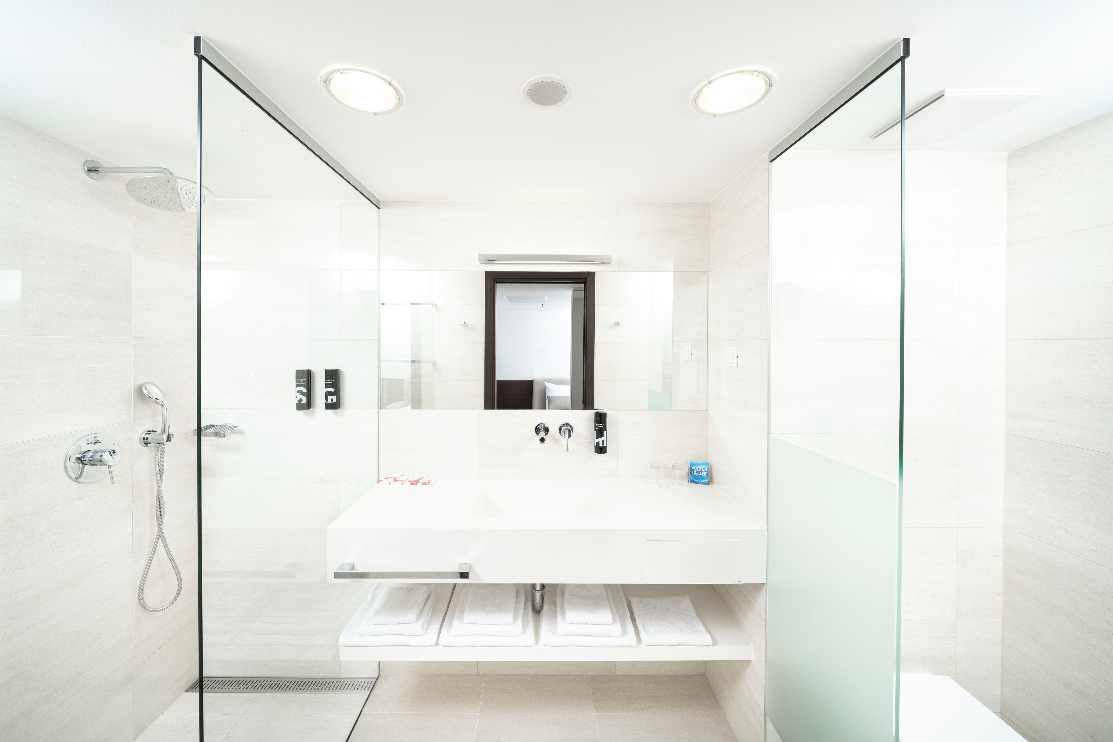 A modern bathroom with a glass-enclosed shower, a white sink with a mirror above, and a towel rack below.