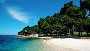 A beach with clear turquoise water, a sandy shore, and a row of trees. - Hotel Parentium Plava Laguna (Porec)