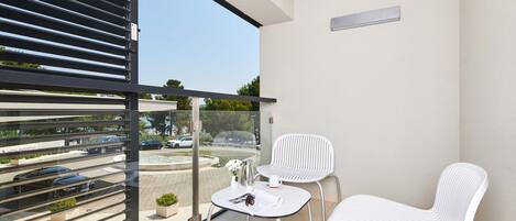 A balcony with a glass door, two white chairs, a small table with a magazine, and a potted plant.