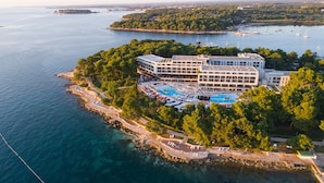 An aerial view of a resort with a large pool, multiple buildings, and a coastline. - Hotel Parentium Plava Laguna (Porec)