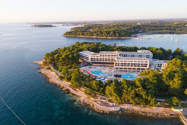 Vista aérea de un complejo turístico con una piscina grande, varias edificaciones y una costa.