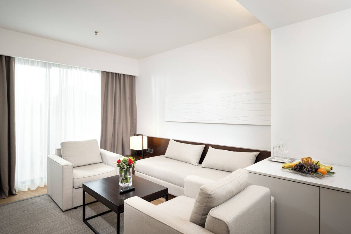 A modern hotel room with a sofa, armchair, and a small table with a vase of flowers.