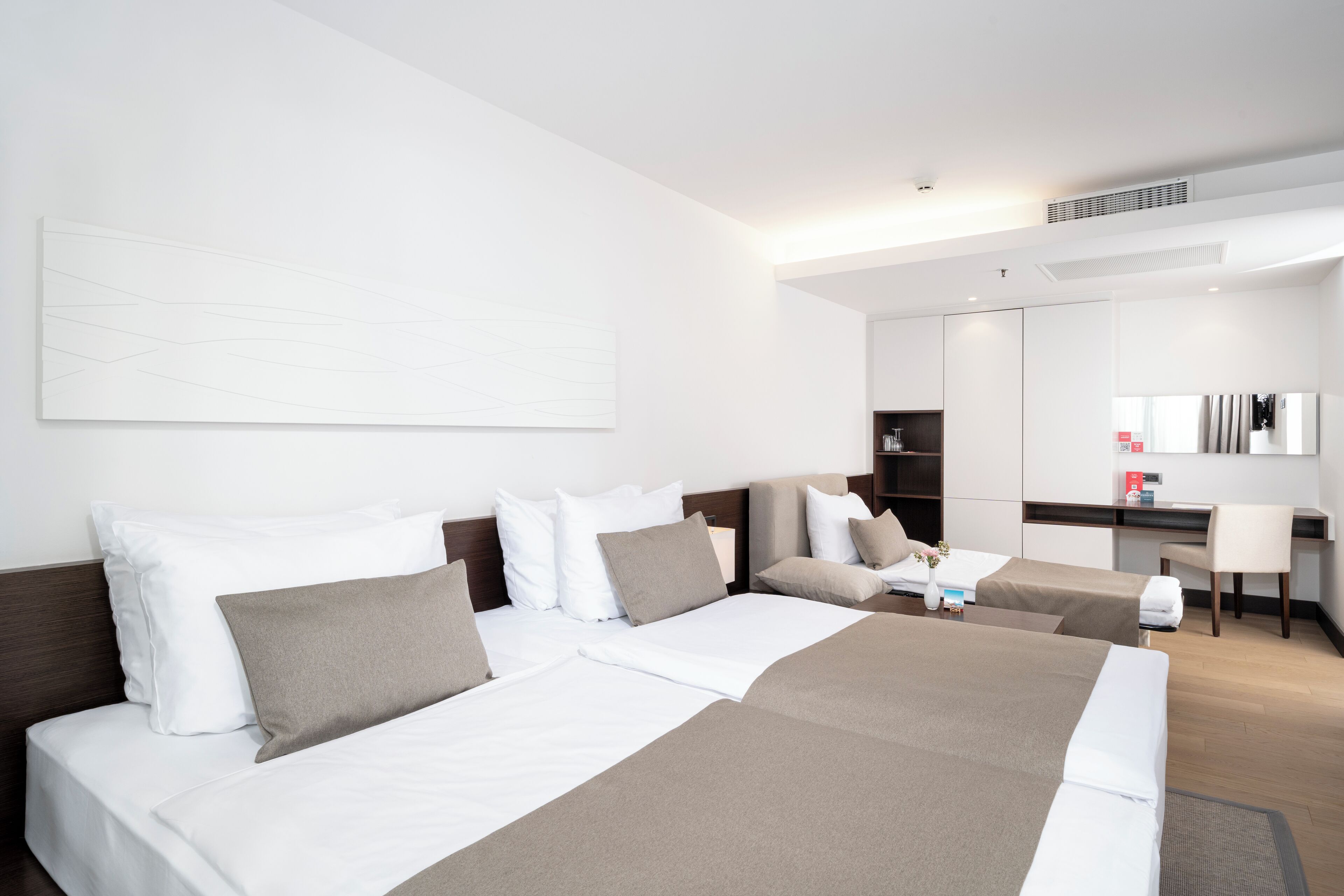 A modern hotel room with two beds, a desk, and a large mirror.