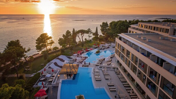 A resort with a large pool, sun loungers, and a view of the sea at sunset. - Hotel Parentium Plava Laguna (Porec)