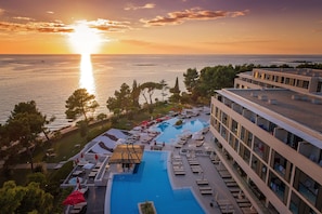 Un resort con una piscina grande, tumbonas y vista al mar al atardecer.
