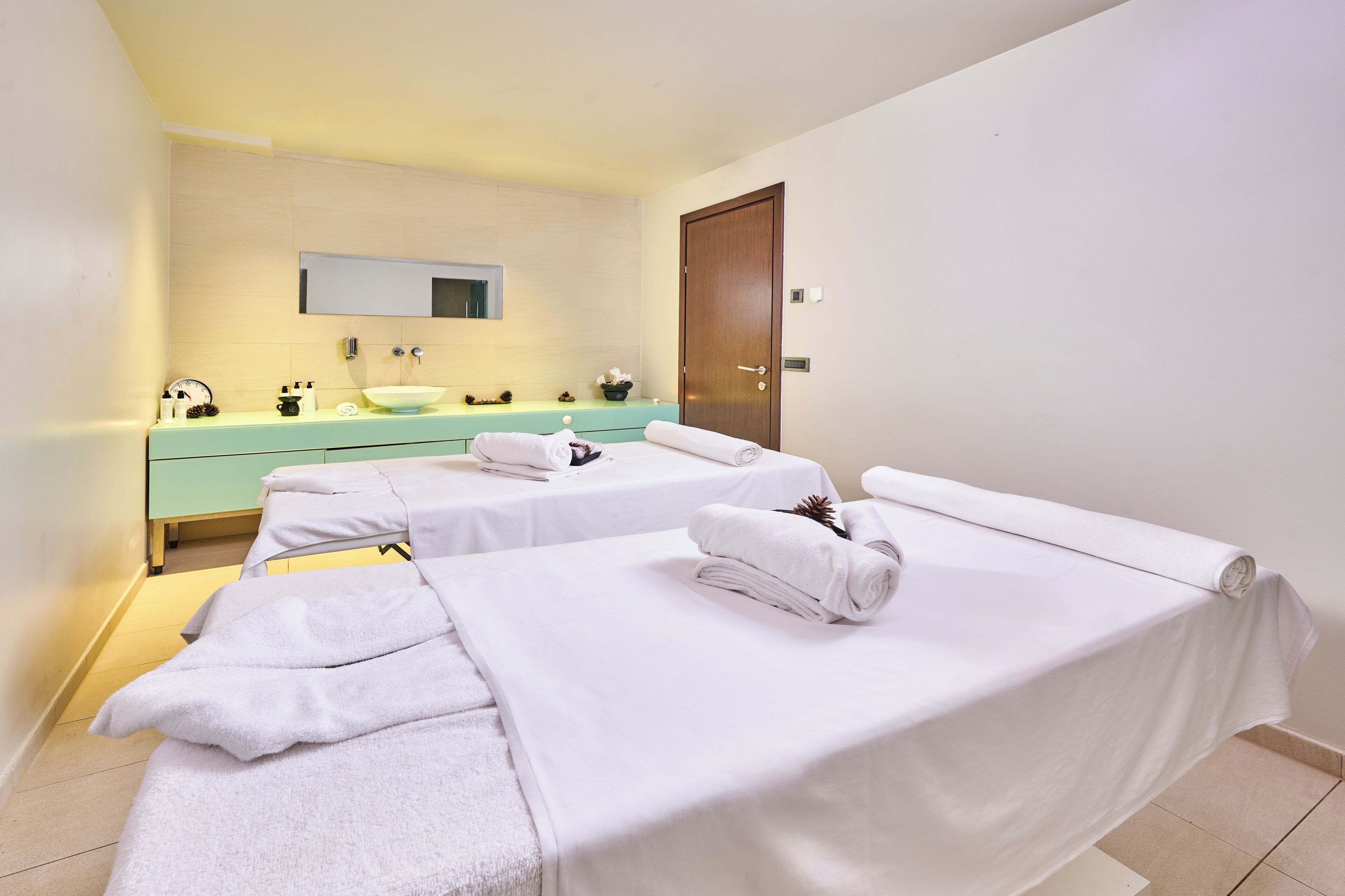 A hotel room with two beds, a bathroom with a sink and mirror, and a wooden door.