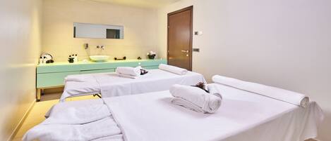 A hotel room with two beds, a bathroom with a sink and mirror, and a wooden door.