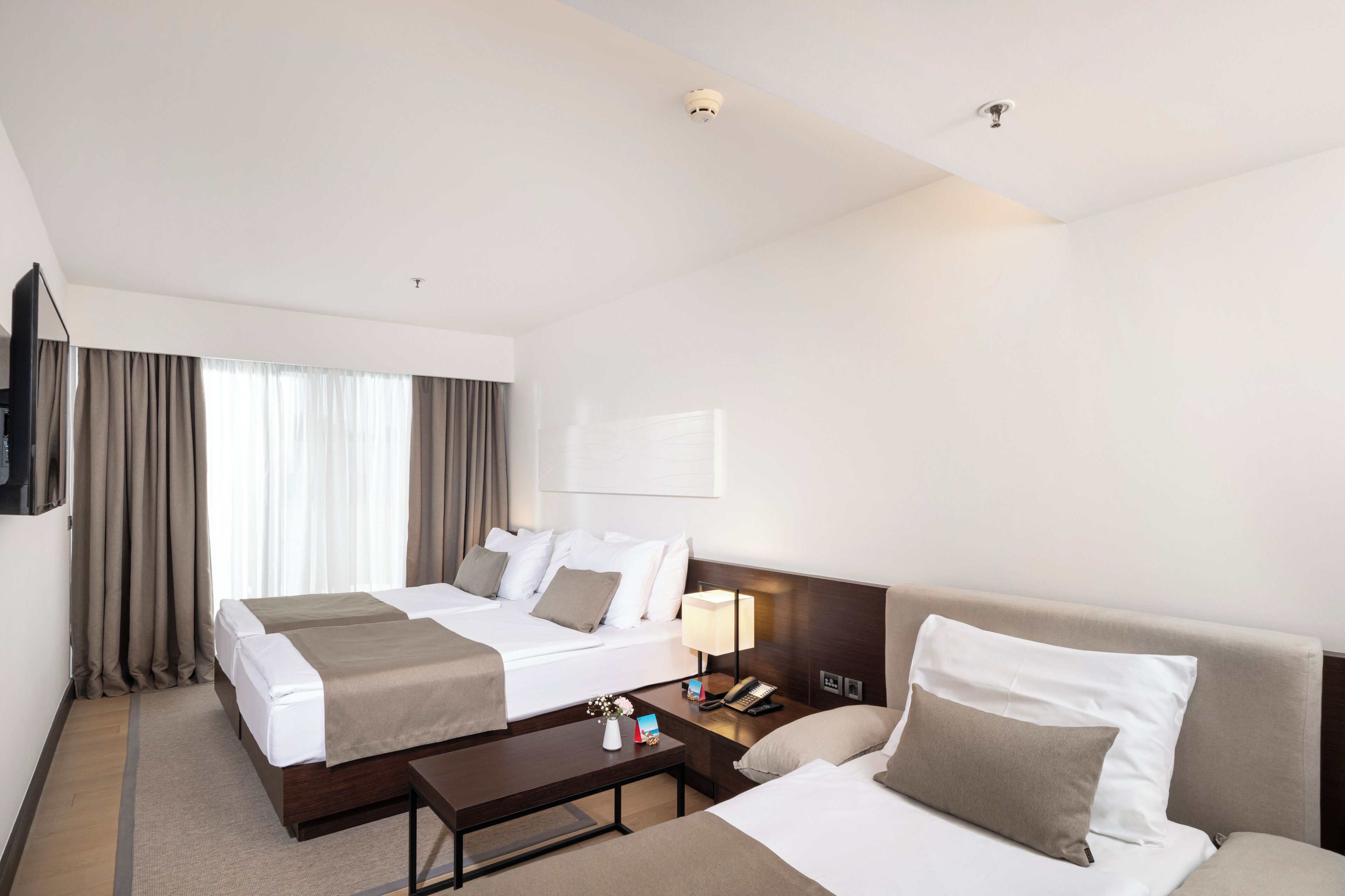 A hotel room with two beds, a sofa, a coffee table, a TV, and a lamp.