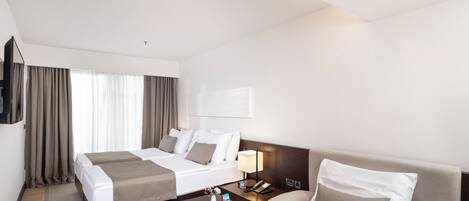 A hotel room with two beds, a sofa, a coffee table, a TV, and a lamp.