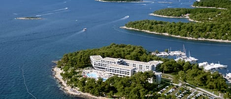 An aerial view of a coastal hotel with a swimming pool, marina, and lush greenery.