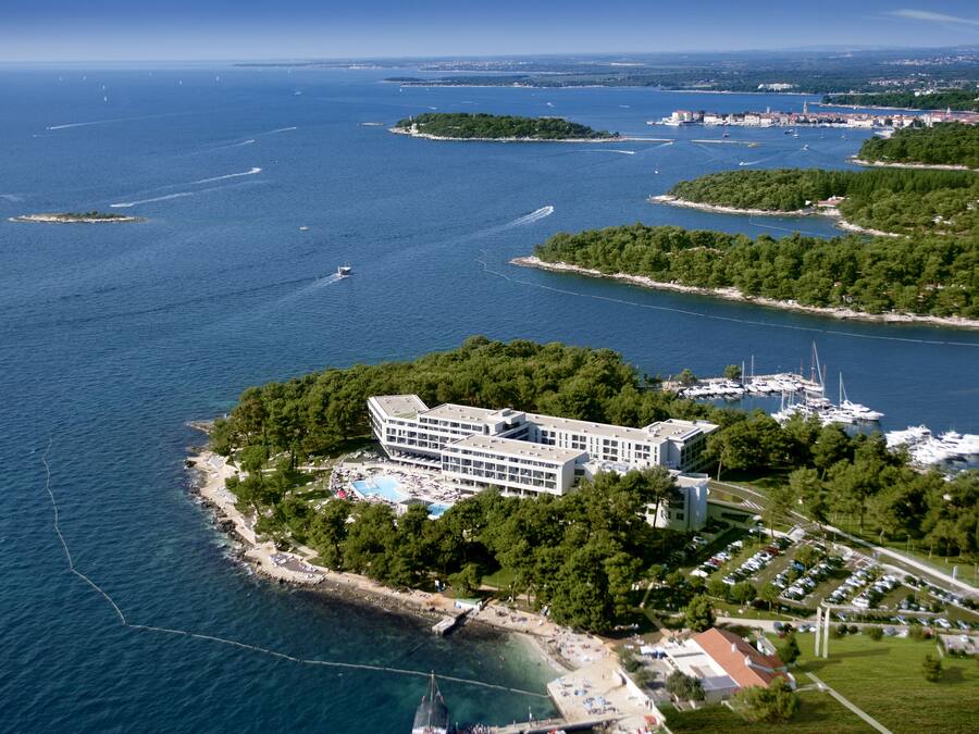 An aerial view of a coastal hotel with a swimming pool, marina, and lush greenery.