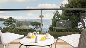 A balcony with a table set for breakfast, overlooking a body of water and greenery. - Hotel Parentium Plava Laguna (Porec)
