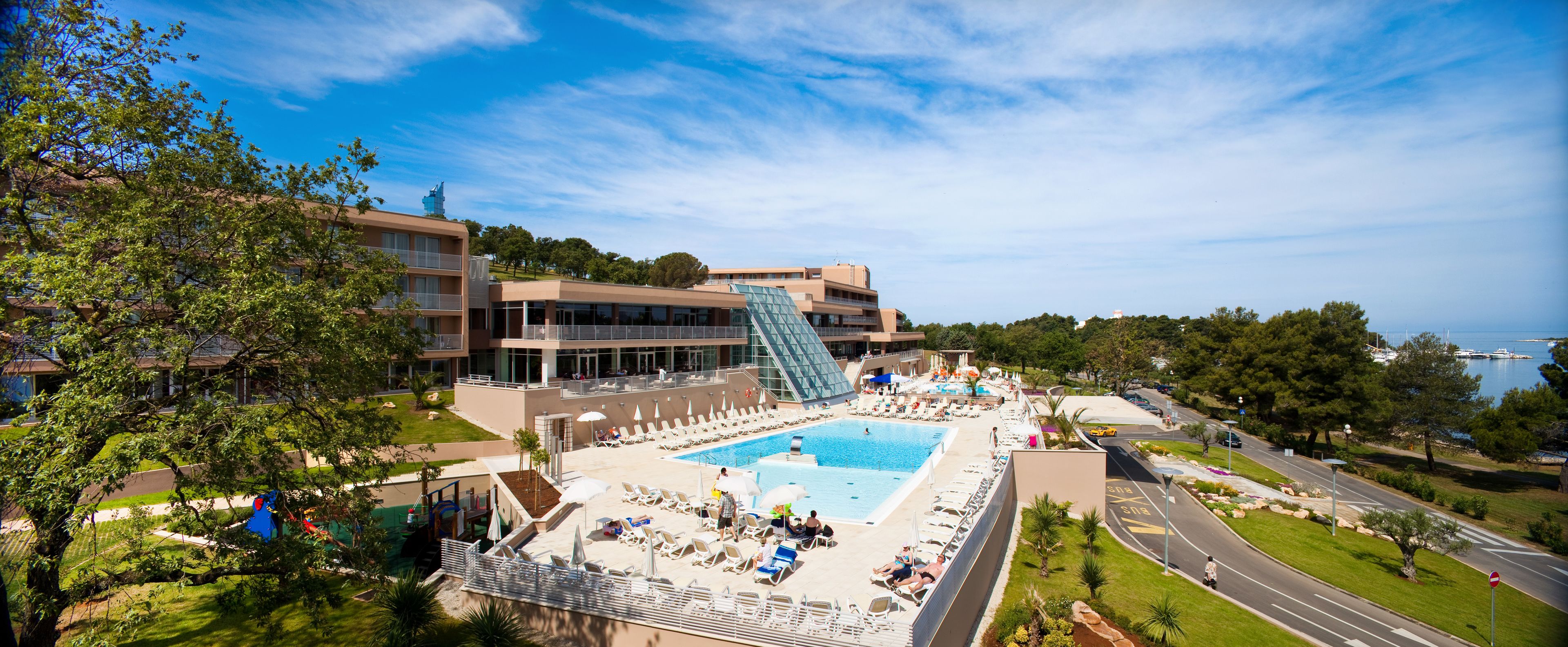 A hotel with a large pool, a glass staircase, and a view of the sea.