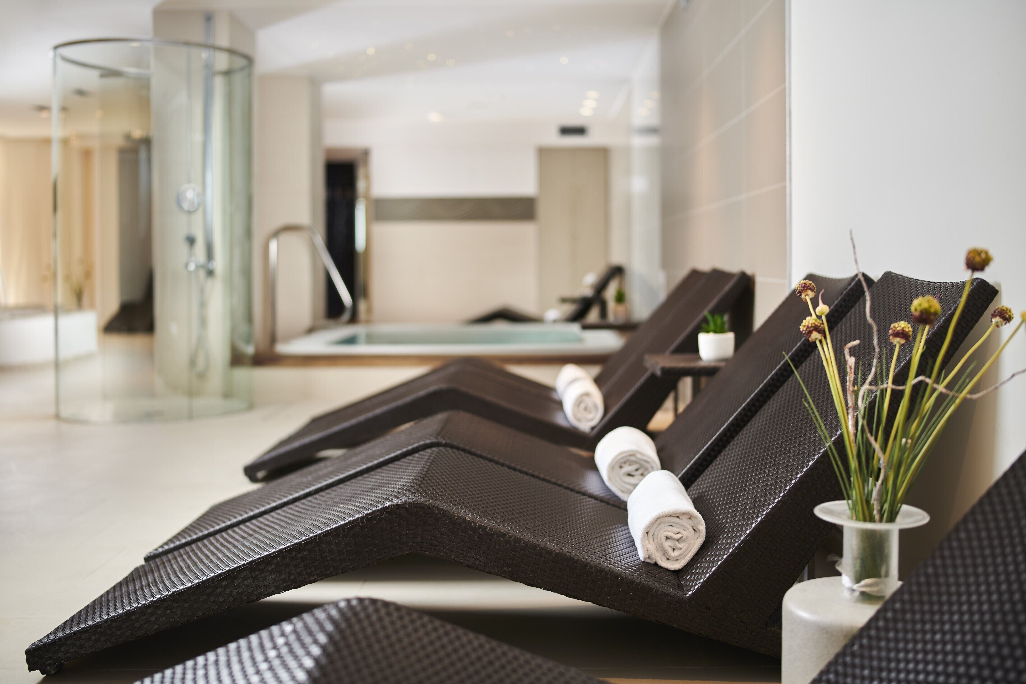Un'area spa moderna con poltrone reclinabili, cabina doccia in vetro e una piccola pianta in vaso.