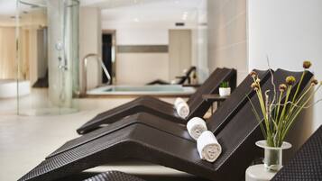 Un'area spa moderna con poltrone reclinabili, cabina doccia in vetro e una piccola pianta in vaso.