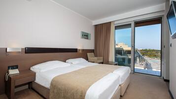 Une chambre d’hôtel avec un grand lit, un bureau avec un téléphone, une chaise, une télévision et un balcon avec vue.