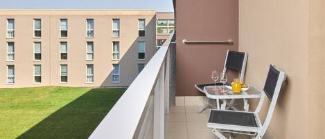 A balcony with a table set for two, a chair, and a glass of wine.