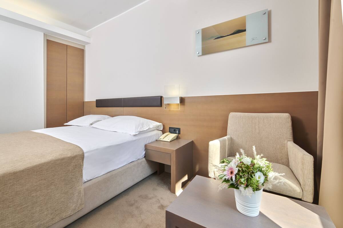 Quarto de hotel com cama, mesa de cabeceira, cadeira e um quadro na parede.