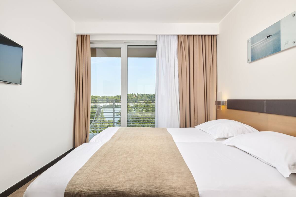 Quarto de hotel com uma cama grande, televisão de tela plana na parede e varanda com cortinas.