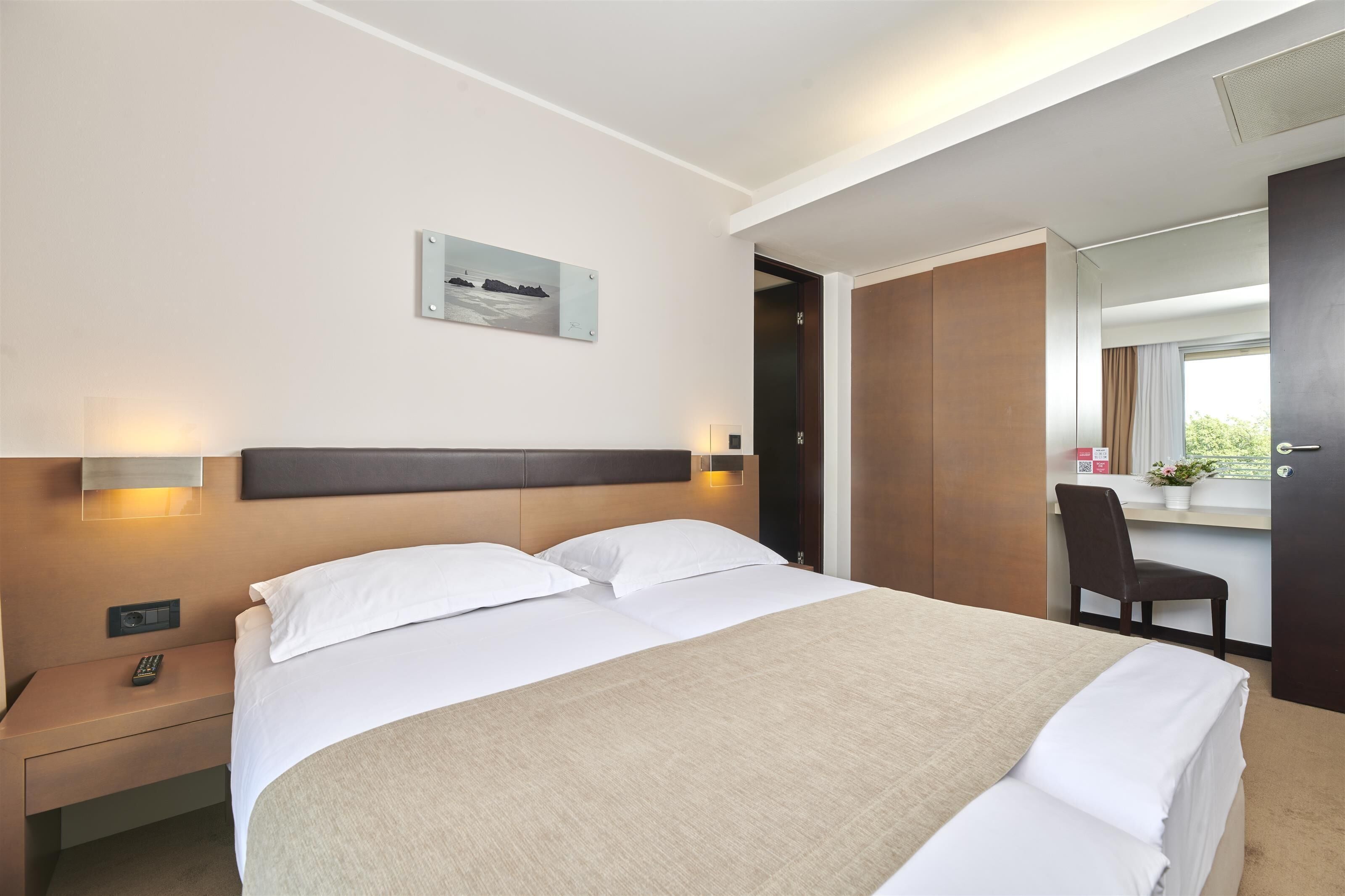 Ein Hotelzimmer mit einem großen Bett, Nachttischen, einem Schreibtisch und einem Sessel.