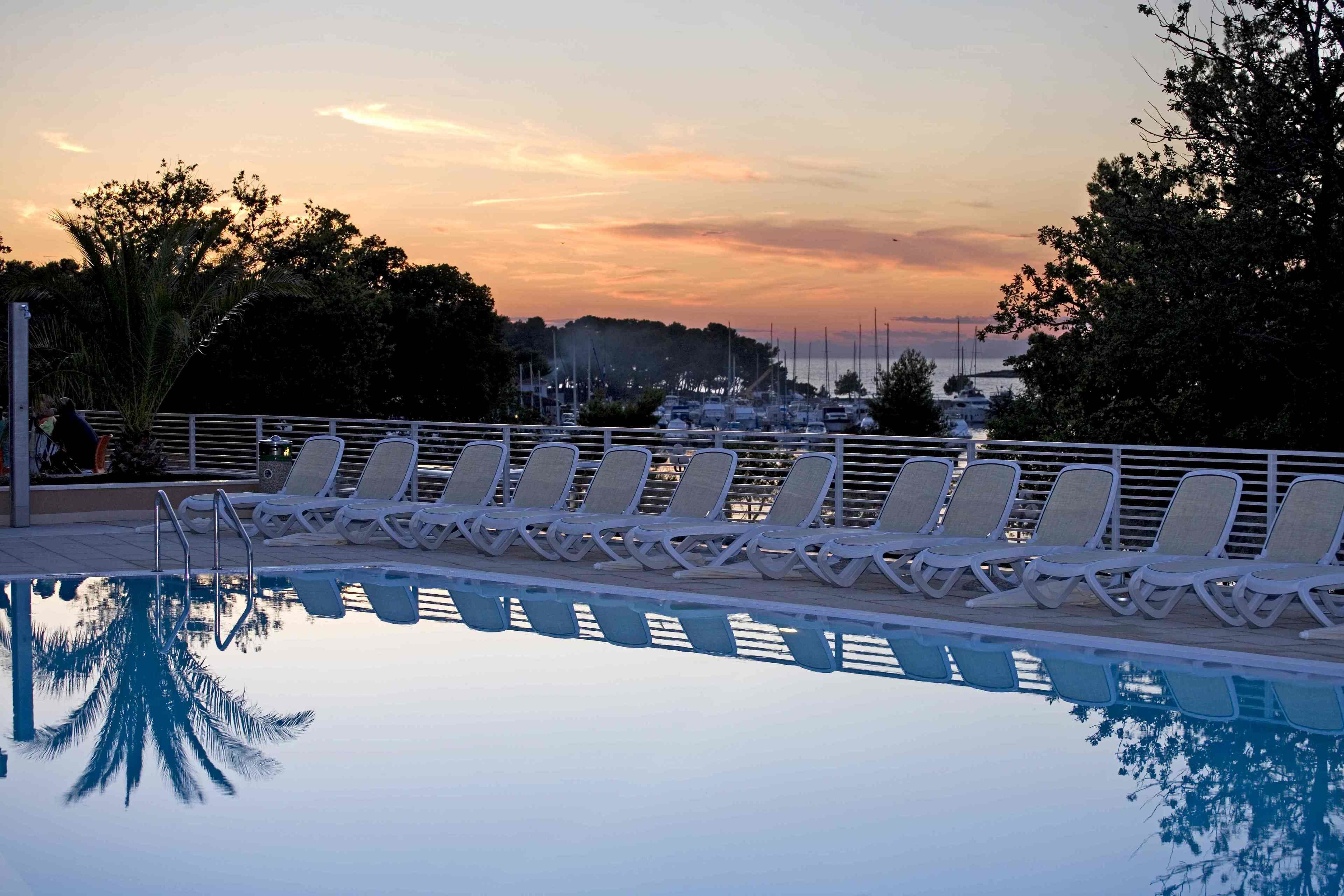 Zona de piscina con sillones de descanso y vistas al puerto al atardecer.