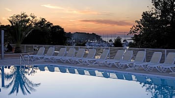 Zona de piscina con sillones de descanso y vistas al puerto al atardecer.