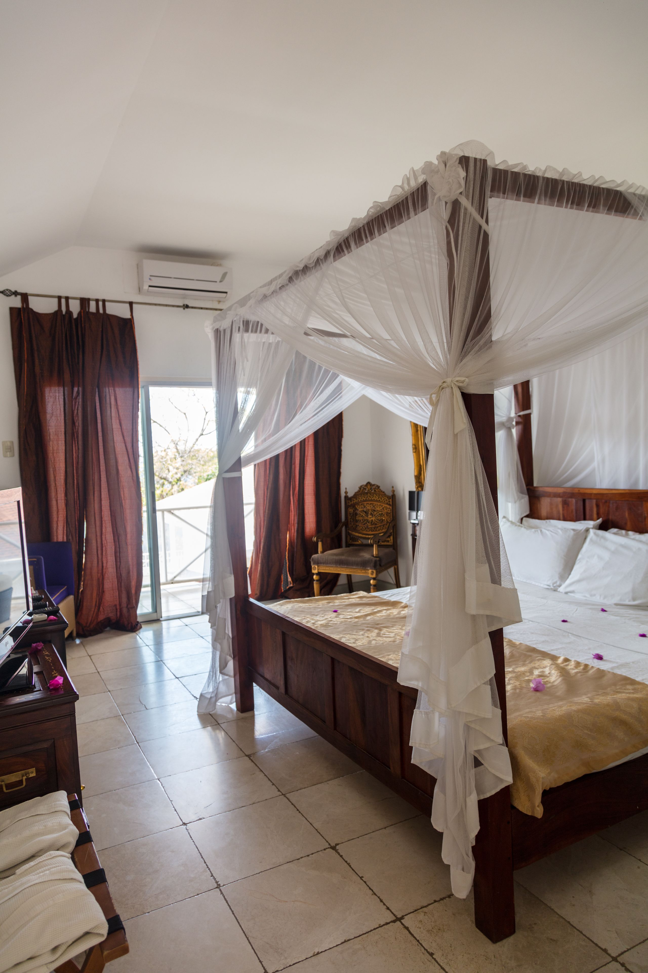 A bedroom with a four-poster bed, a wooden chair, and a desk with a lamp.