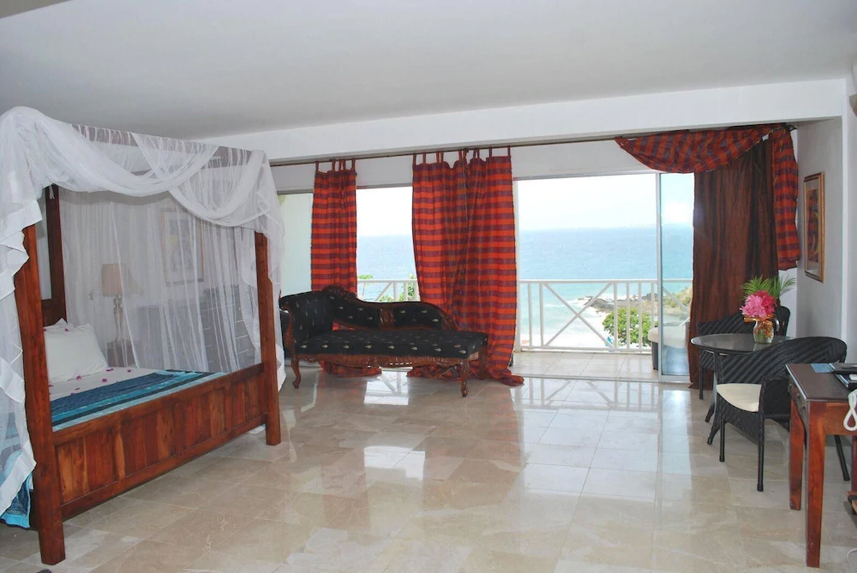 Un dormitorio con cama con dosel, un sofá, una mesa de comedor y vistas al mar.