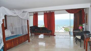 Un dormitorio con cama con dosel, un sofá, una mesa de comedor y vistas al mar.