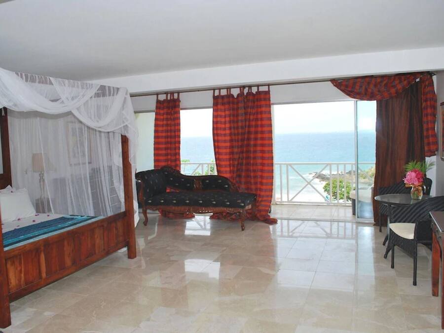 Un dormitorio con cama con dosel, un sofá, una mesa de comedor y vistas al mar.