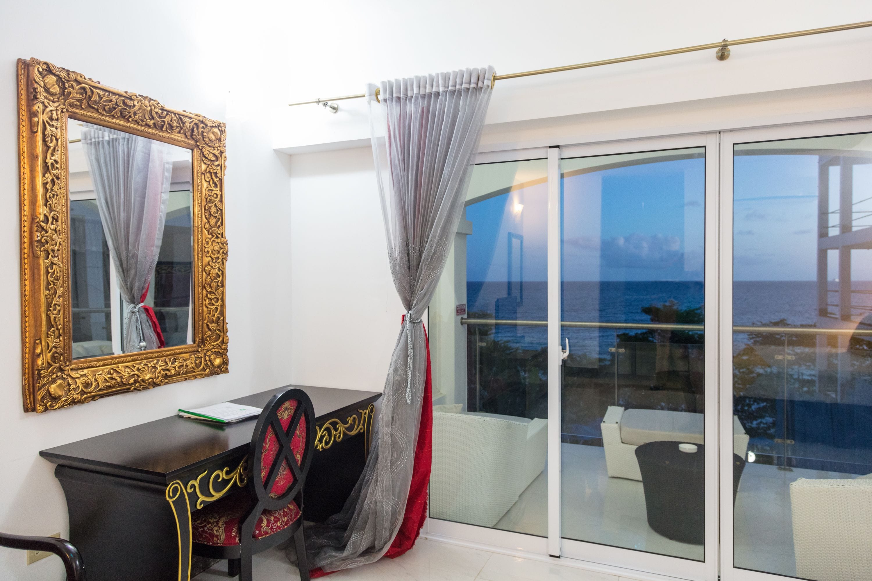 Une pièce dotée d’un grand miroir, d’un bureau avec une chaise, et offrant une vue sur la mer grâce à une porte-fenêtre coulissante.