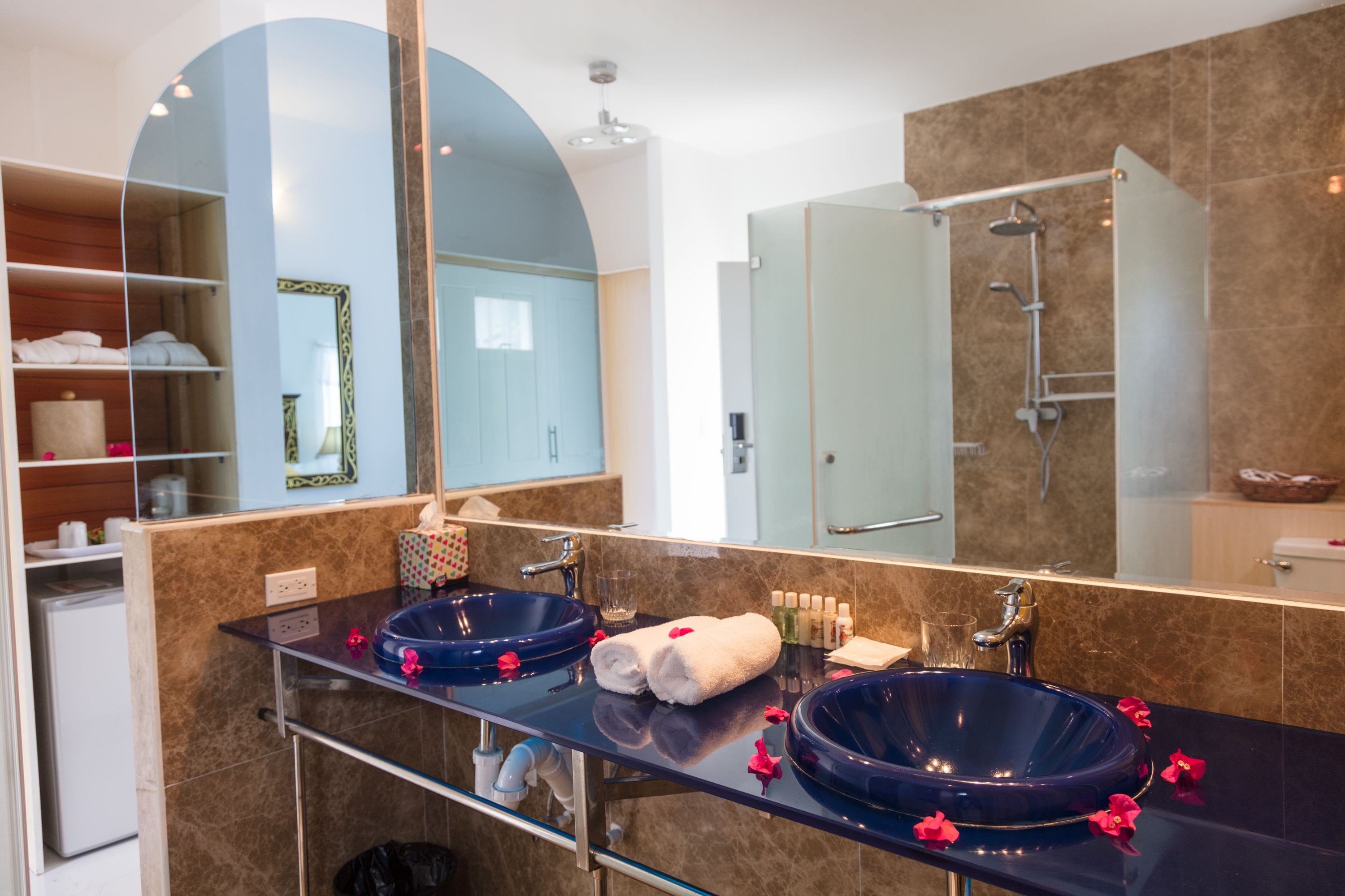 A modern bathroom with two large blue sinks, a glass shower enclosure, and a large mirror.