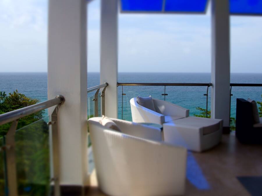 Een balkon met uitzicht op de oceaan, witte meubels en een glazen hekwerk.