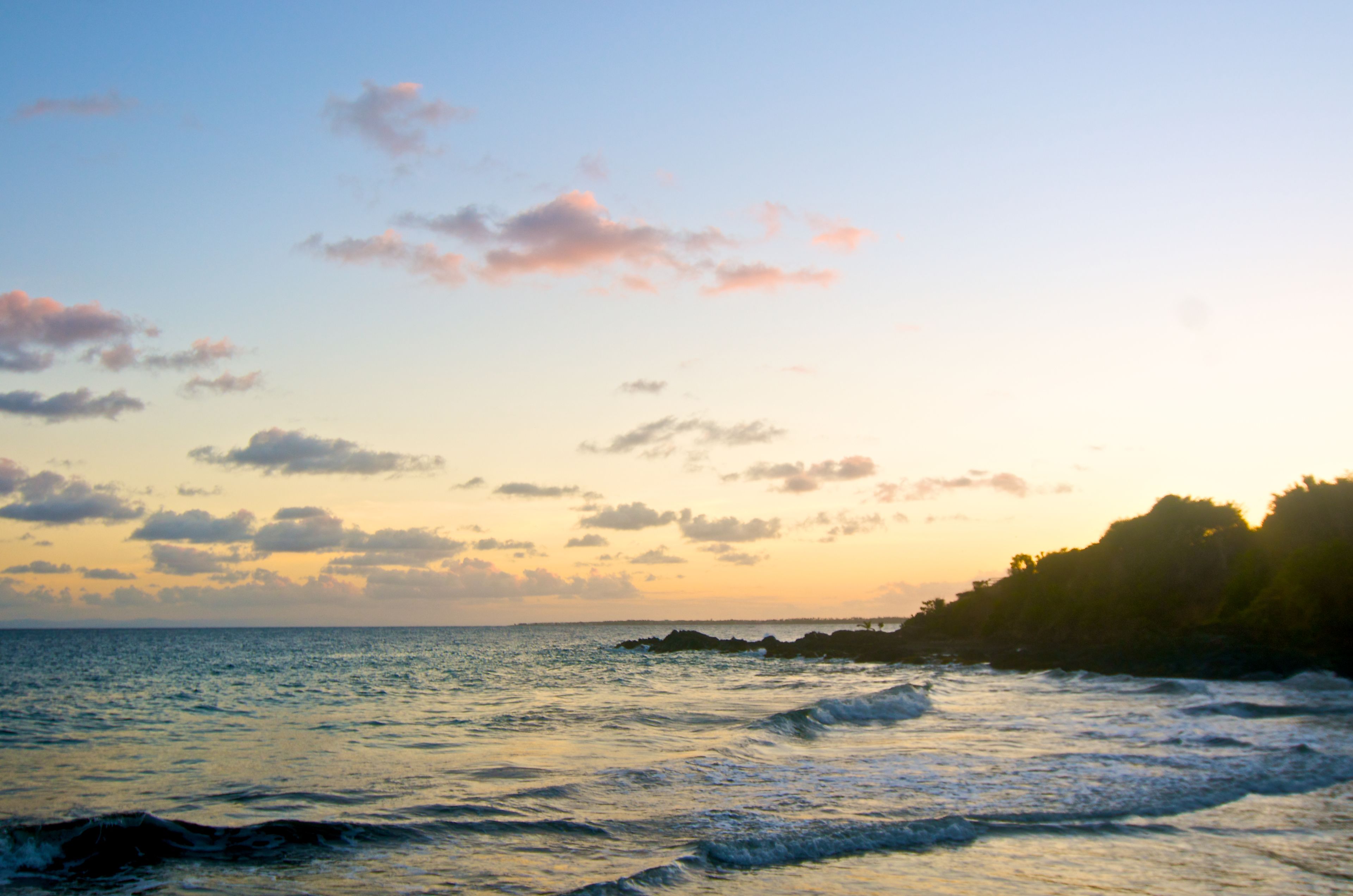 A coastal landscape with a clear sky, calm sea, and rocky shoreline.