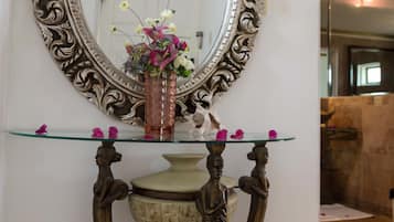 A mirror with an ornate frame, a glass table with a vase of flowers, and a decorative base.