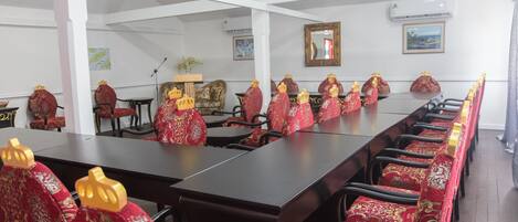 Een congreszaal met een lange tafel en rijen stoelen met rode en gouden patronen.