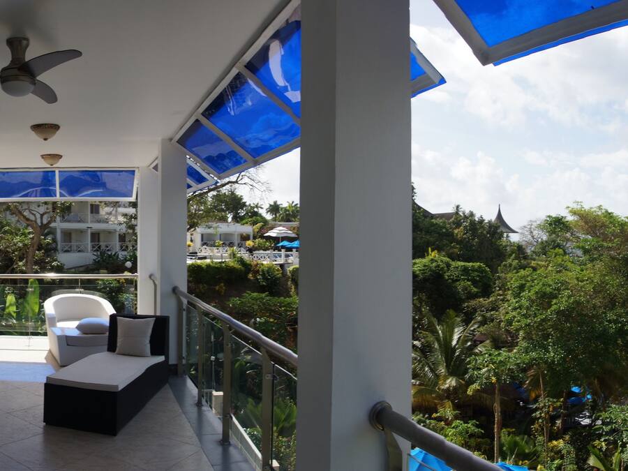 A balcony with a glass railing, a ceiling fan, and a view of the ocean and greenery.