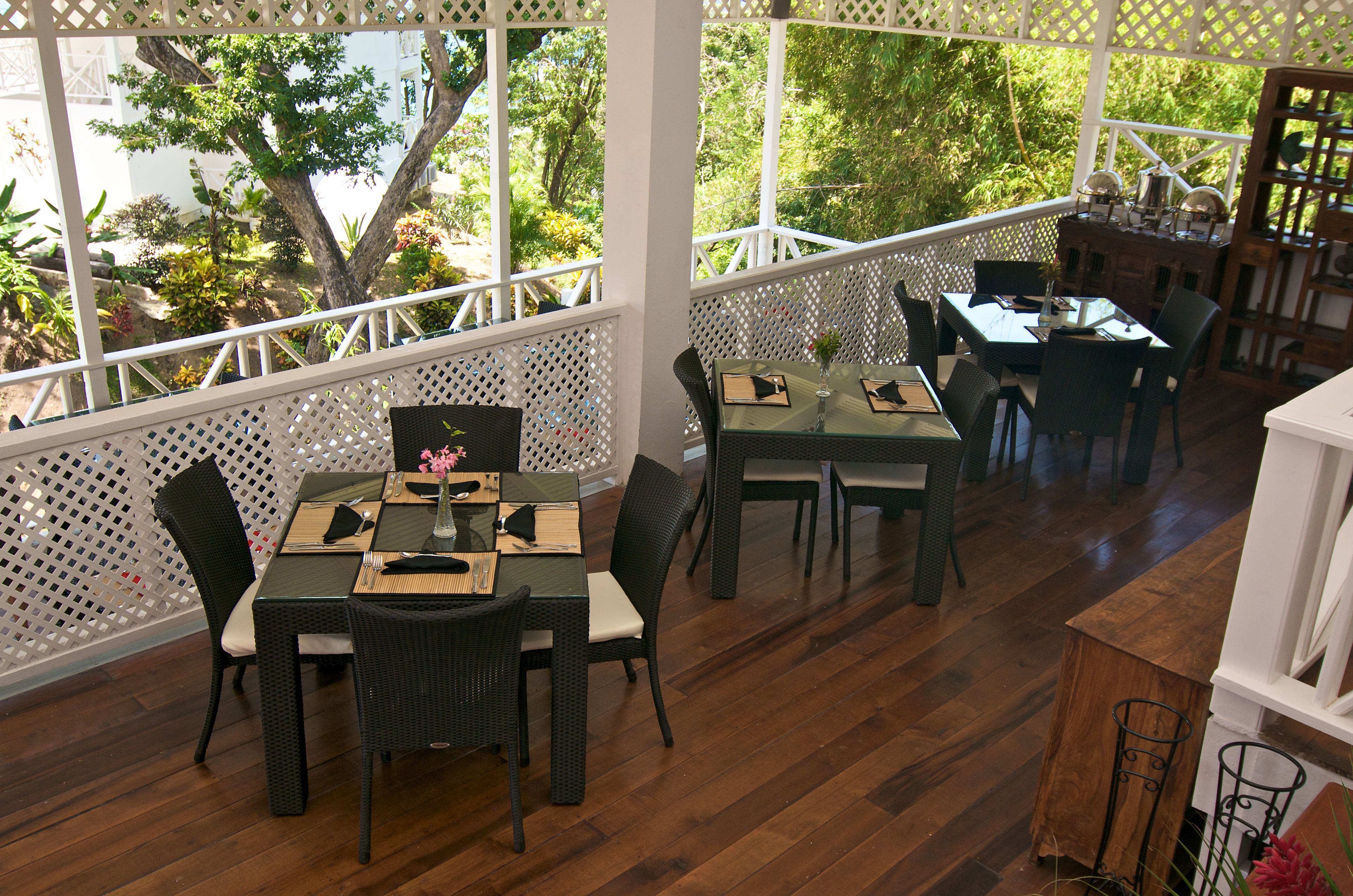 A dining area with tables and chairs, wooden flooring, and a view of greenery outside.